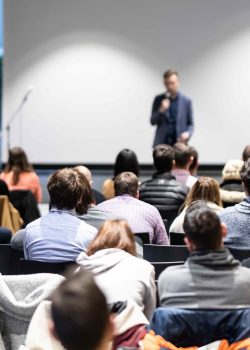 Speaker giving a talk in conference hall at business event. Audience at the conference hall. Business and Entrepreneurship concept. Focus on unrecognizable people in audience.