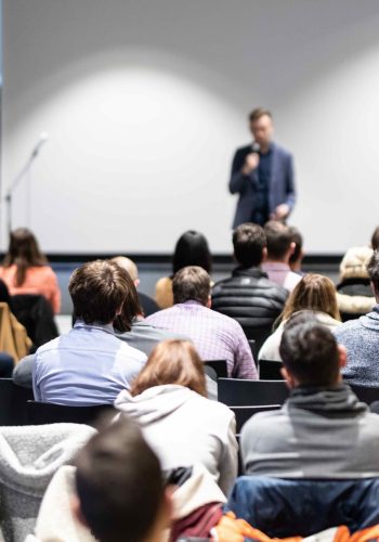 Speaker giving a talk in conference hall at business event. Audience at the conference hall. Business and Entrepreneurship concept. Focus on unrecognizable people in audience.